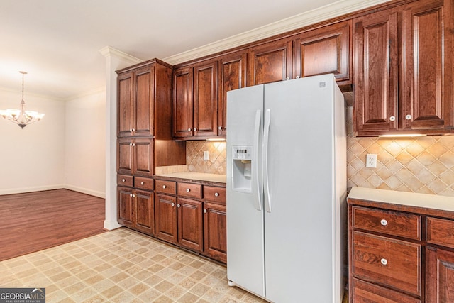 kitchen featuring ornamental molding, backsplash, white fridge with ice dispenser, baseboards, and a chandelier