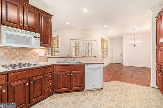 kitchen with crown molding, decorative backsplash, a notable chandelier, white appliances, and a sink