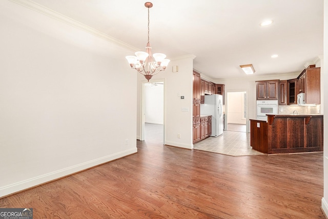 kitchen featuring white appliances, a peninsula, light wood-type flooring, and a chandelier