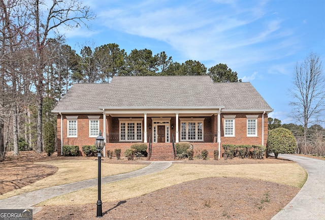 ranch-style home with a porch, brick siding, and roof with shingles