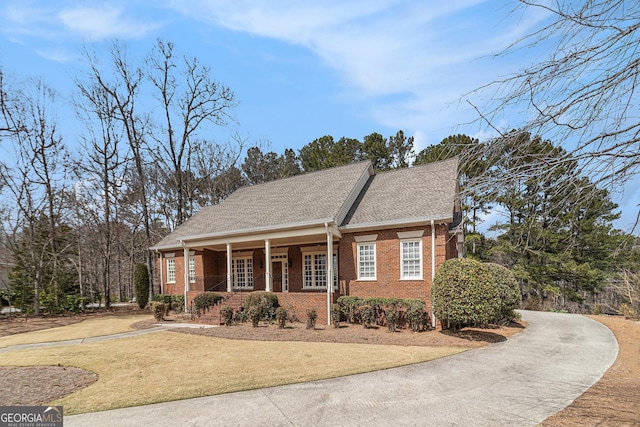 view of front of home featuring brick siding, a porch, a front yard, roof with shingles, and driveway