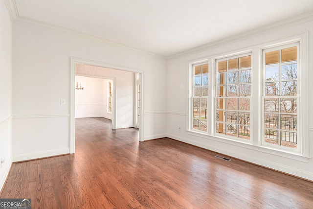 empty room featuring visible vents, crown molding, baseboards, and wood finished floors