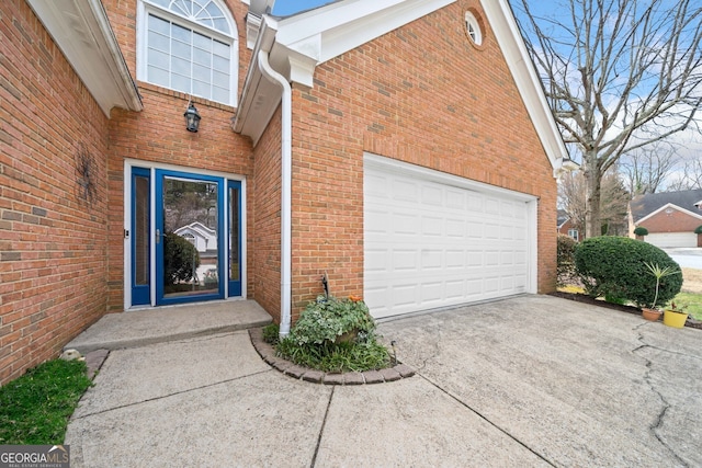 doorway to property with a garage, brick siding, and concrete driveway