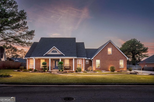 view of front of home with brick siding, fence, and a lawn