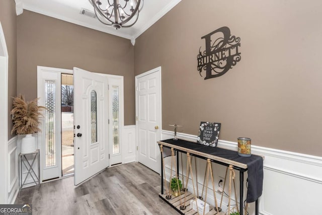 foyer featuring visible vents, a chandelier, a wainscoted wall, ornamental molding, and wood finished floors