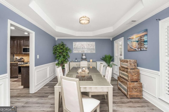 dining area with a raised ceiling, light wood-style flooring, and wainscoting