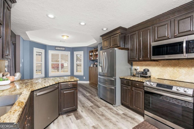 kitchen with stainless steel appliances, a raised ceiling, dark brown cabinetry, and light wood finished floors