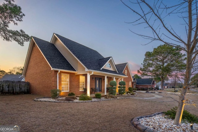 view of front facade featuring brick siding, roof with shingles, covered porch, and fence