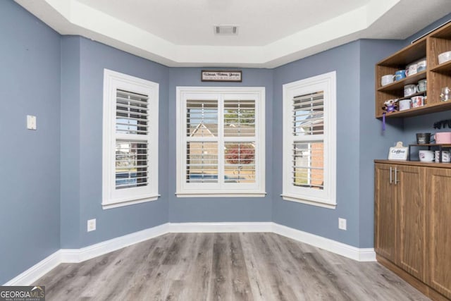 unfurnished dining area featuring visible vents, baseboards, a tray ceiling, and wood finished floors