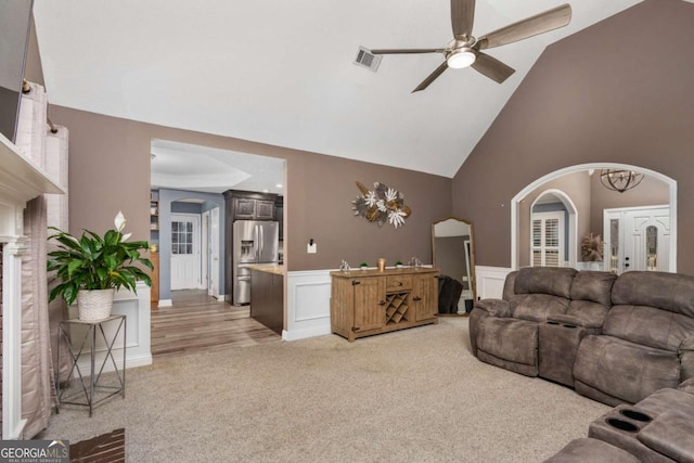 living room featuring light carpet, a wainscoted wall, arched walkways, and ceiling fan