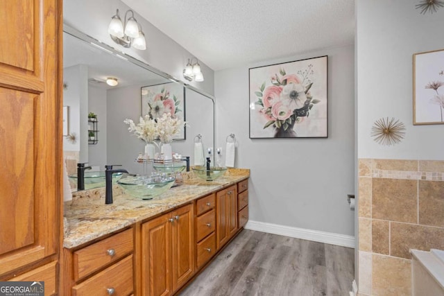 full bath with baseboards, double vanity, wood finished floors, a textured ceiling, and a sink