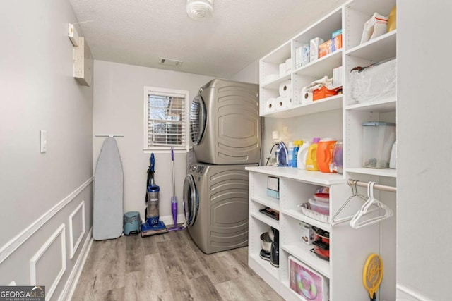 washroom with light wood finished floors, stacked washer / dryer, visible vents, laundry area, and a textured ceiling