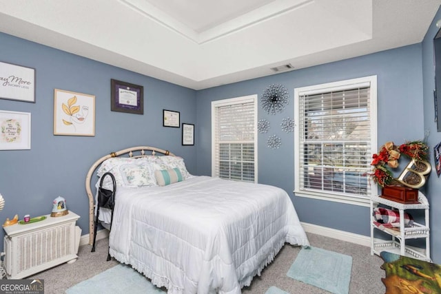 carpeted bedroom with visible vents, a raised ceiling, and baseboards