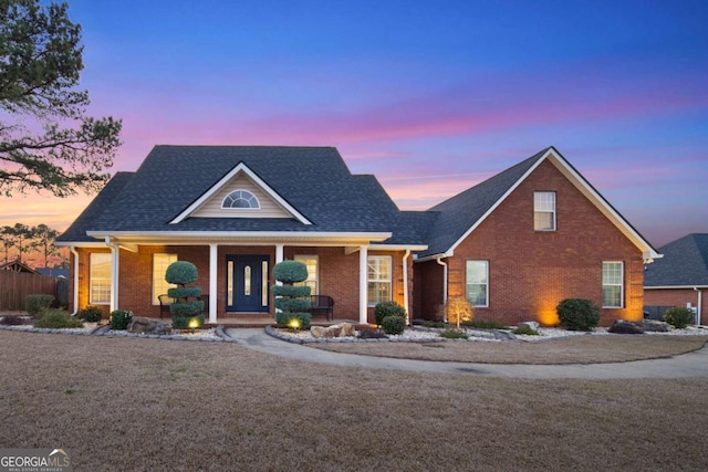 traditional-style home featuring brick siding, covered porch, roof with shingles, and fence