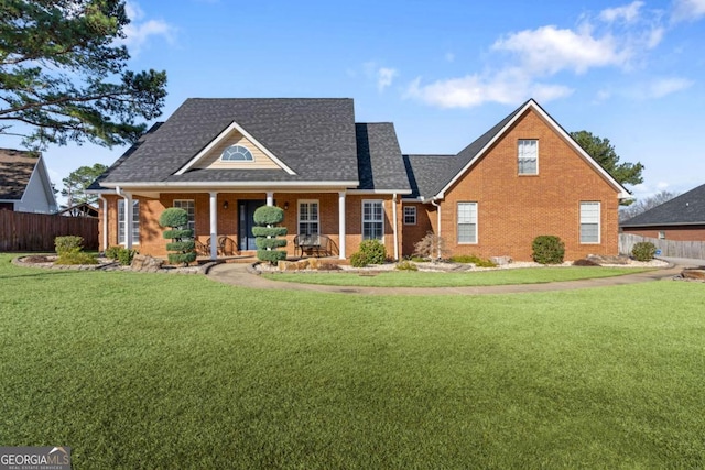 view of front facade featuring a front yard, fence, a porch, a shingled roof, and brick siding