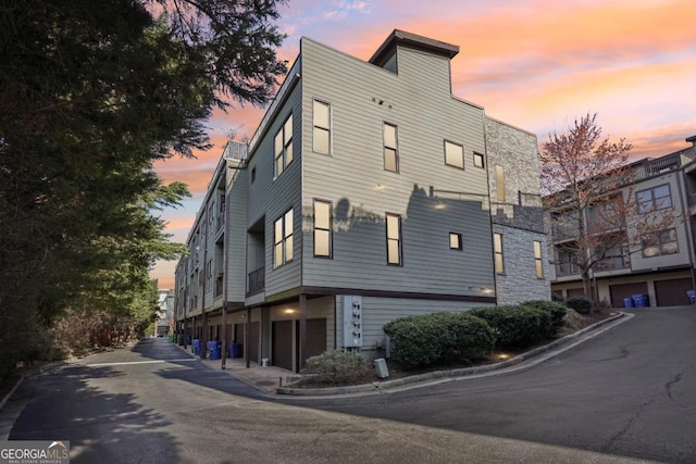 1199 Huff Rd Unit 121, Atlanta, GA 30318 - property exterior at dusk with an attached garage, stone siding, and driveway