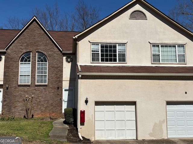 view of front facade with stucco siding, brick siding, and an attached garage