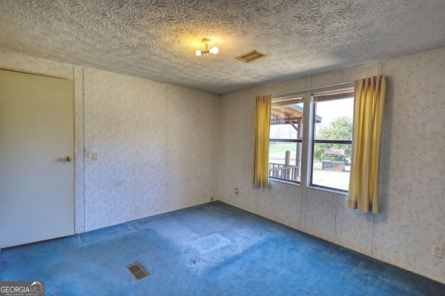 carpeted empty room featuring visible vents, wallpapered walls, and a textured ceiling