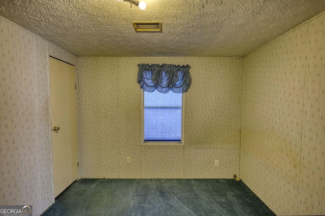 unfurnished room with visible vents, dark carpet, and a textured ceiling