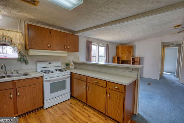 kitchen with a peninsula, gas range gas stove, a sink, a textured ceiling, and brown cabinets