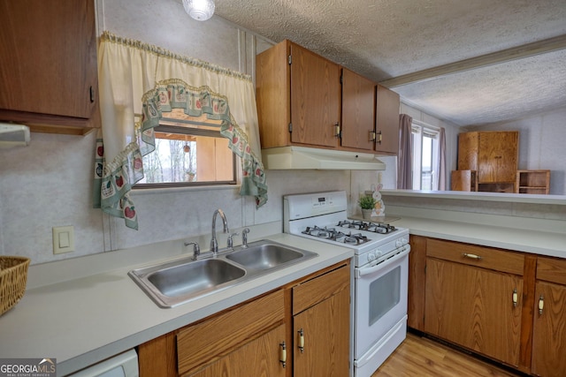 kitchen with under cabinet range hood, a sink, a textured ceiling, white gas range oven, and light countertops