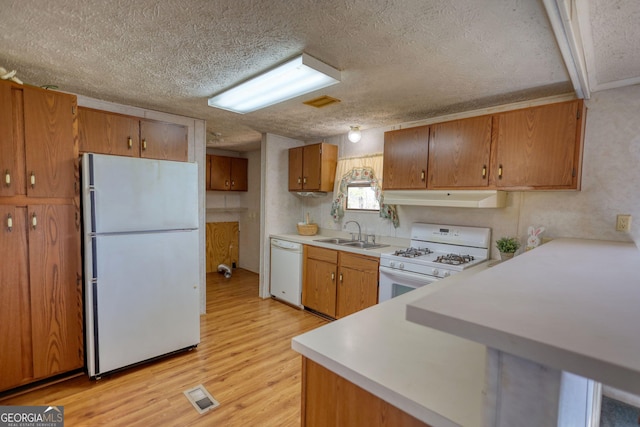 kitchen with under cabinet range hood, white appliances, light countertops, and a sink