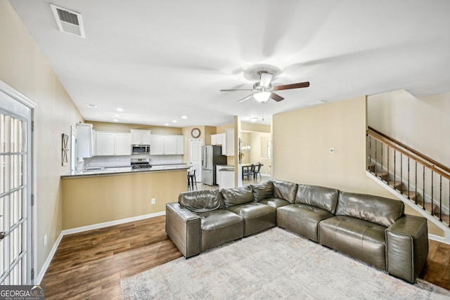 living area with visible vents, a ceiling fan, wood finished floors, stairway, and baseboards