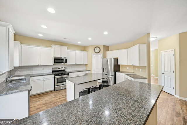 kitchen with light wood-style flooring, a sink, a center island, stainless steel appliances, and decorative backsplash