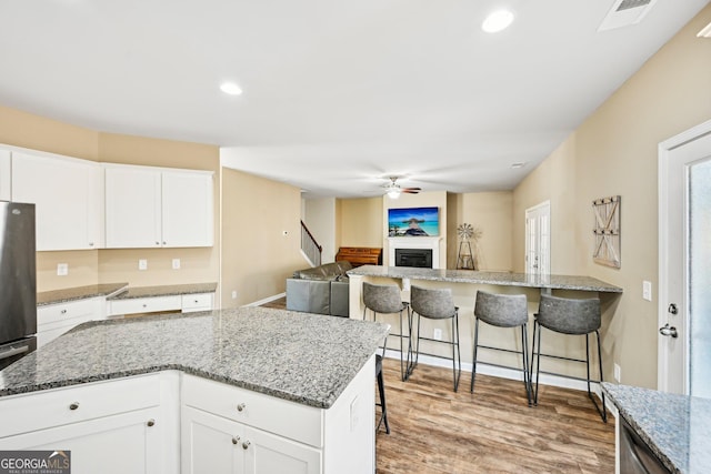 kitchen featuring visible vents, a kitchen bar, a ceiling fan, a fireplace, and light wood finished floors