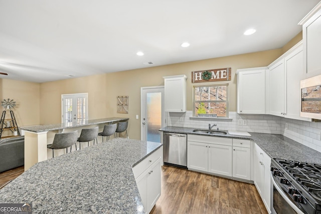 kitchen featuring a sink, backsplash, dark wood-style floors, stainless steel appliances, and a breakfast bar area