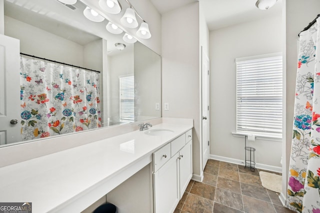 full bathroom featuring vanity, stone finish floor, a healthy amount of sunlight, and baseboards