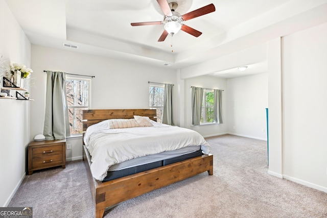 carpeted bedroom with a tray ceiling, baseboards, visible vents, and a ceiling fan