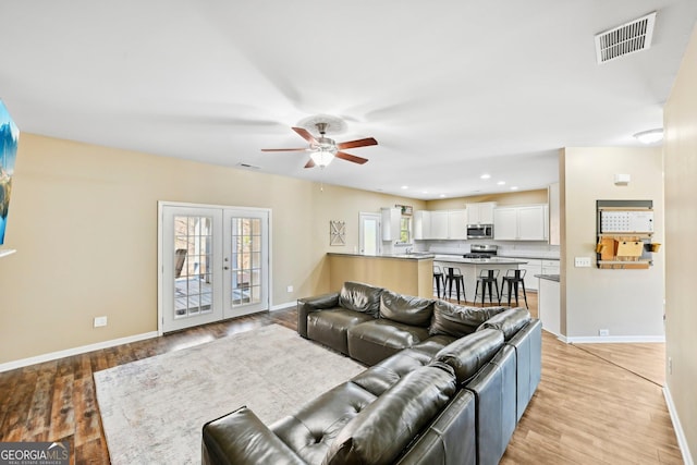 living area featuring a ceiling fan, visible vents, and light wood finished floors