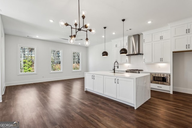 kitchen featuring a sink, white cabinets, stainless steel microwave, wall chimney range hood, and a notable chandelier