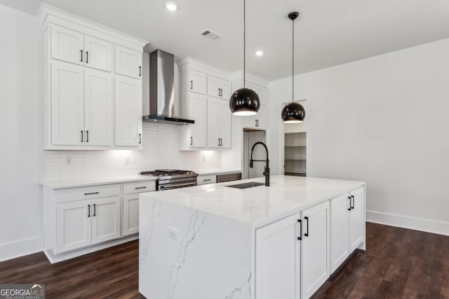 kitchen with visible vents, white cabinets, stainless steel gas range, wall chimney exhaust hood, and a sink