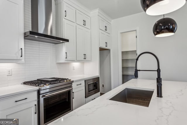 kitchen featuring a sink, white cabinetry, appliances with stainless steel finishes, wall chimney exhaust hood, and decorative backsplash