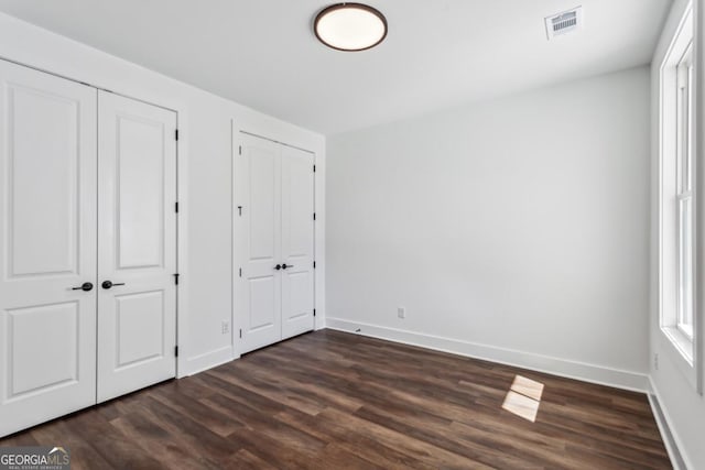 unfurnished bedroom featuring visible vents, baseboards, two closets, and dark wood-style floors