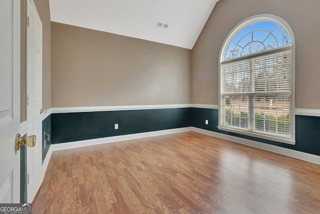 spare room with vaulted ceiling, plenty of natural light, wood finished floors, and visible vents