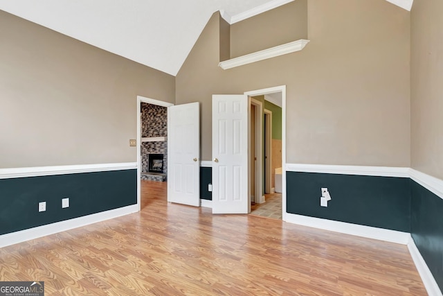 spare room featuring light wood-style flooring, a fireplace with raised hearth, baseboards, and high vaulted ceiling