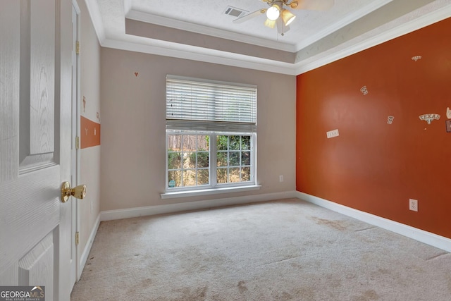 empty room featuring carpet, visible vents, ceiling fan, ornamental molding, and a raised ceiling