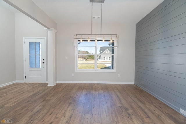 unfurnished dining area with wooden walls, wood finished floors, visible vents, and baseboards