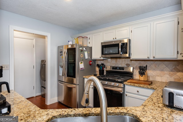 kitchen with a sink, backsplash, appliances with stainless steel finishes, and white cabinetry