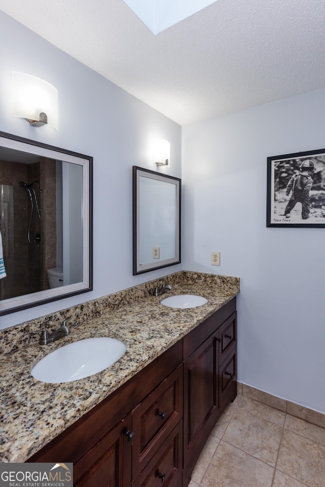 full bathroom featuring double vanity, toilet, a tile shower, and a sink