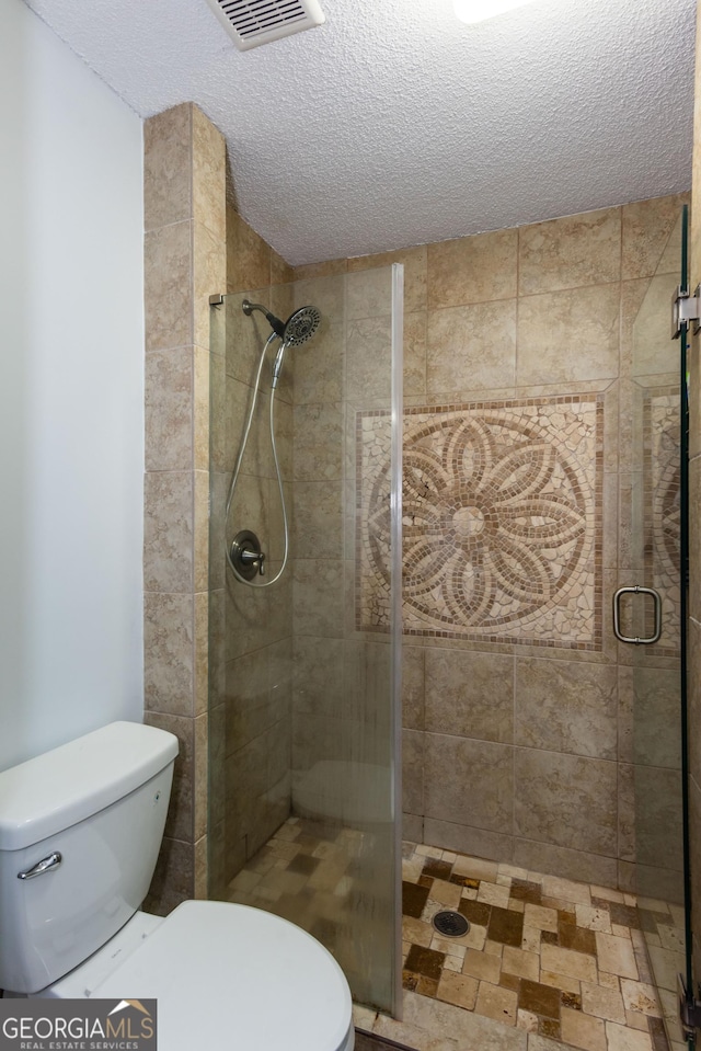 full bathroom featuring visible vents, toilet, a stall shower, and a textured ceiling