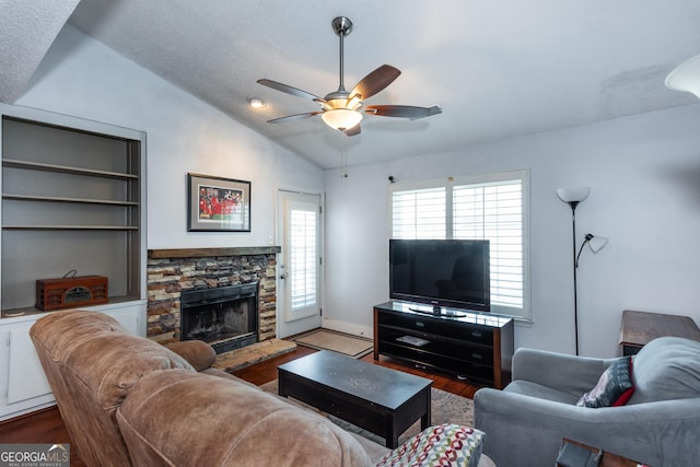 living room with a ceiling fan, a textured ceiling, wood finished floors, a stone fireplace, and vaulted ceiling