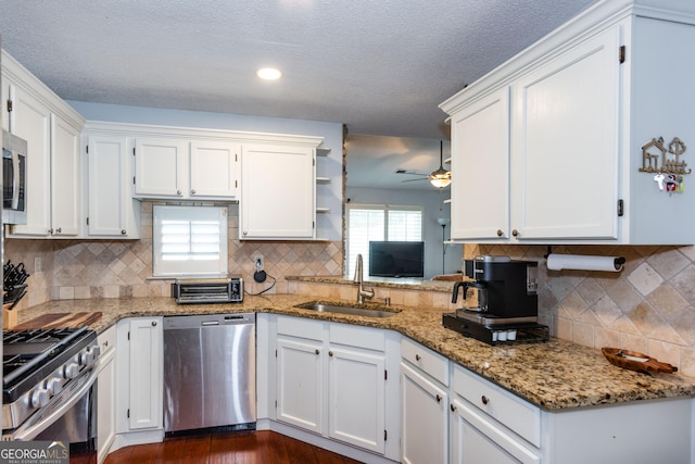 kitchen with a sink, light stone counters, appliances with stainless steel finishes, white cabinets, and ceiling fan