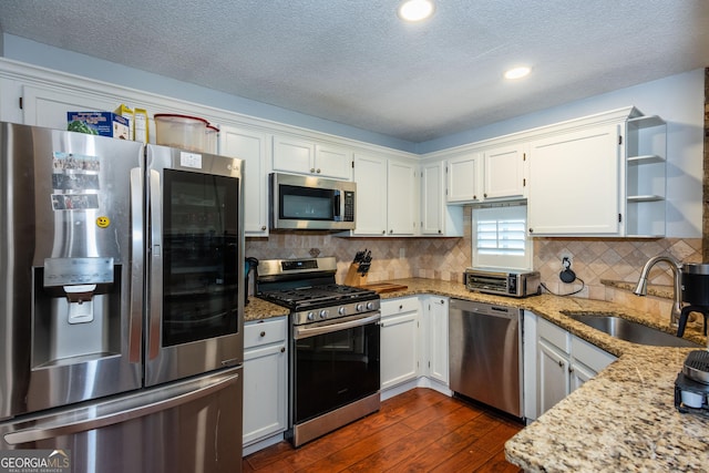 kitchen with dark wood-type flooring, a sink, light stone counters, stainless steel appliances, and white cabinets