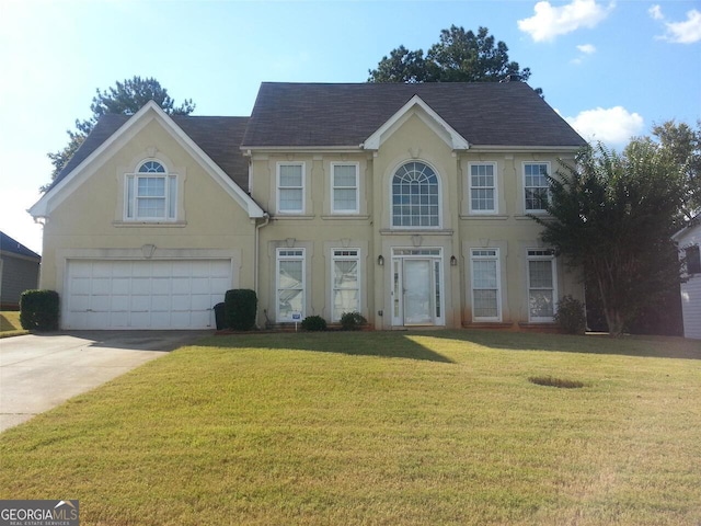 colonial-style house featuring stucco siding, driveway, a front lawn, an attached garage, and a shingled roof