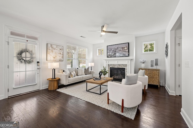 living area featuring a wealth of natural light, a fireplace, ceiling fan, and dark wood-style flooring