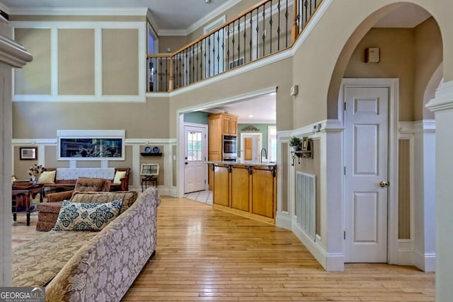 living area featuring light wood-type flooring, visible vents, arched walkways, a high ceiling, and crown molding